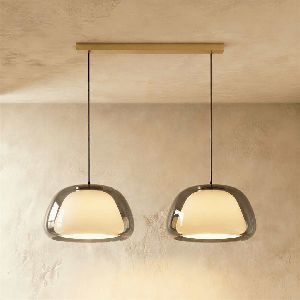 Clérachic two-head pendant light with larger smoked grey glass shades over opal diffusers, on a long brass bar canopy.