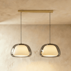 Clérachic two-head pendant light with larger smoked grey glass shades over opal diffusers, on a long brass bar canopy.