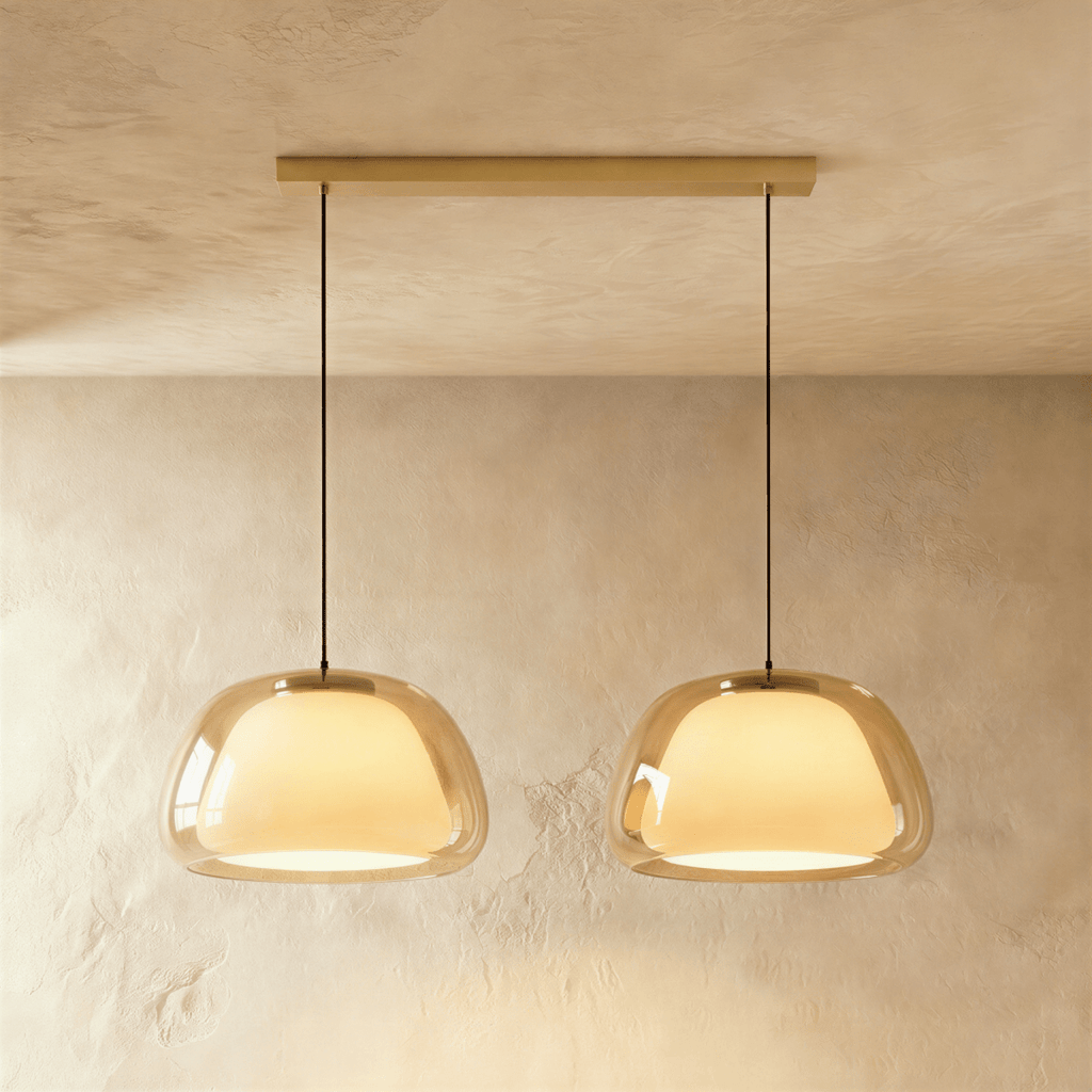 Clérachic two-head pendant light with larger amber glass shades over glowing opal diffusers, on a long brass bar canopy.
