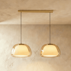 Clérachic two-head pendant light with larger amber glass shades over glowing opal diffusers, on a long brass bar canopy.