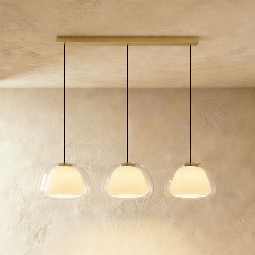 Clérachic three-head pendant light with clear glass shades and opal diffusers in a row from a long brass bar canopy.
