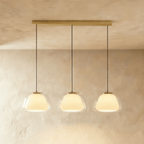 Clérachic three-head pendant light with clear glass shades and opal diffusers in a row from a long brass bar canopy.