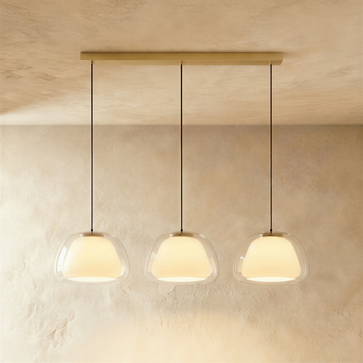 Clérachic three-head pendant light with clear glass shades and opal diffusers in a row from a long brass bar canopy.
