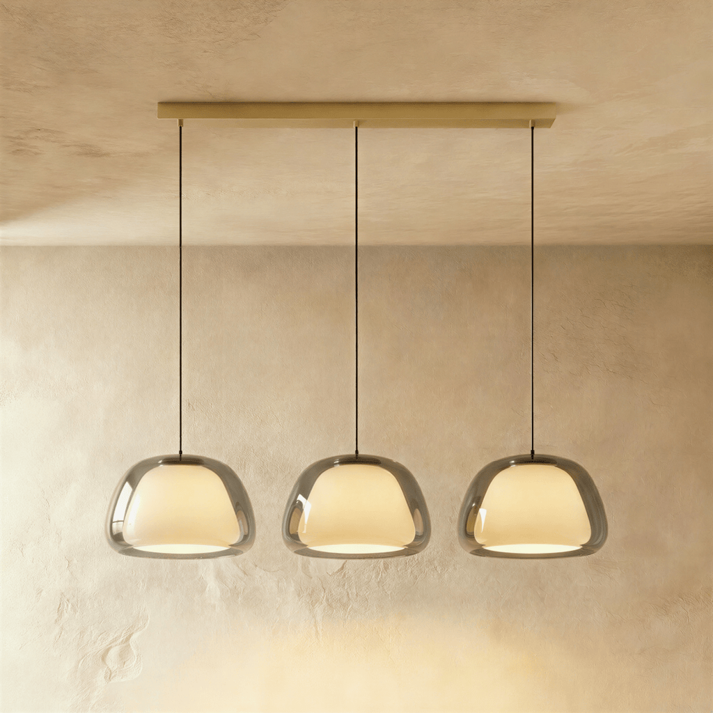 Clérachic three-head pendant light in smoked grey glass with glowing opal diffusers, hung in a row from a brass bar canopy.
