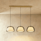 Clérachic three-head pendant light in smoked grey glass with glowing opal diffusers, hung in a row from a brass bar canopy.