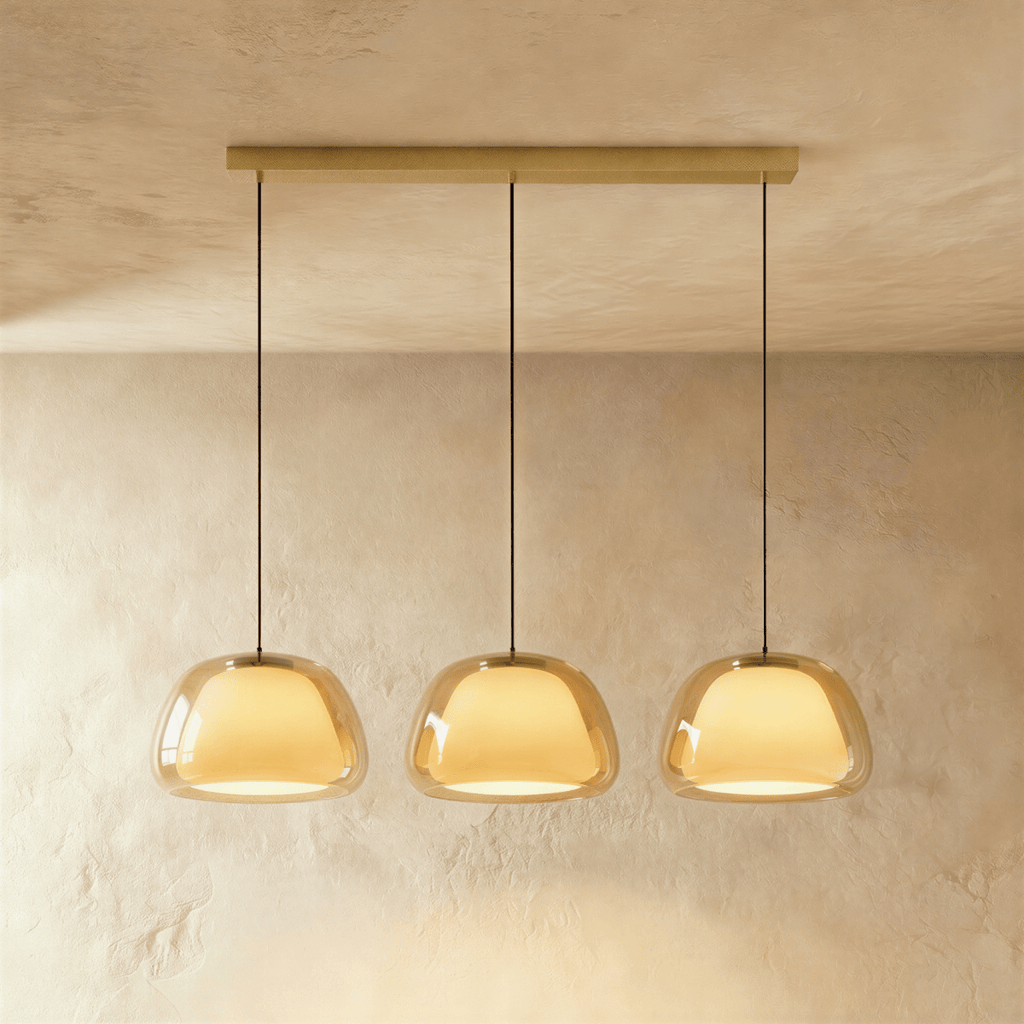 Clérachic three-head pendant light in amber glass with glowing opal diffusers, hung in a row from a brass bar canopy.
