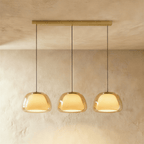 Clérachic three-head pendant light in amber glass with glowing opal diffusers, hung in a row from a brass bar canopy.