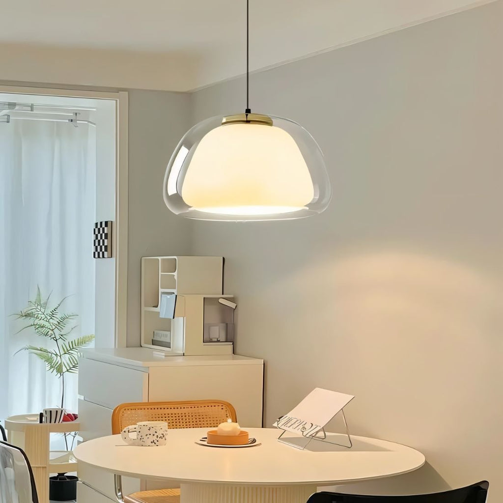 Clérachic clear glass pendant light over a round white dining table, its opal inner shade glowing in a bright, airy corner.