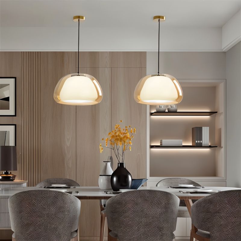 Clérachic pair of amber glass pendant lights with opal diffusers above a dining table, beside oak panelling and a lit shelf.
