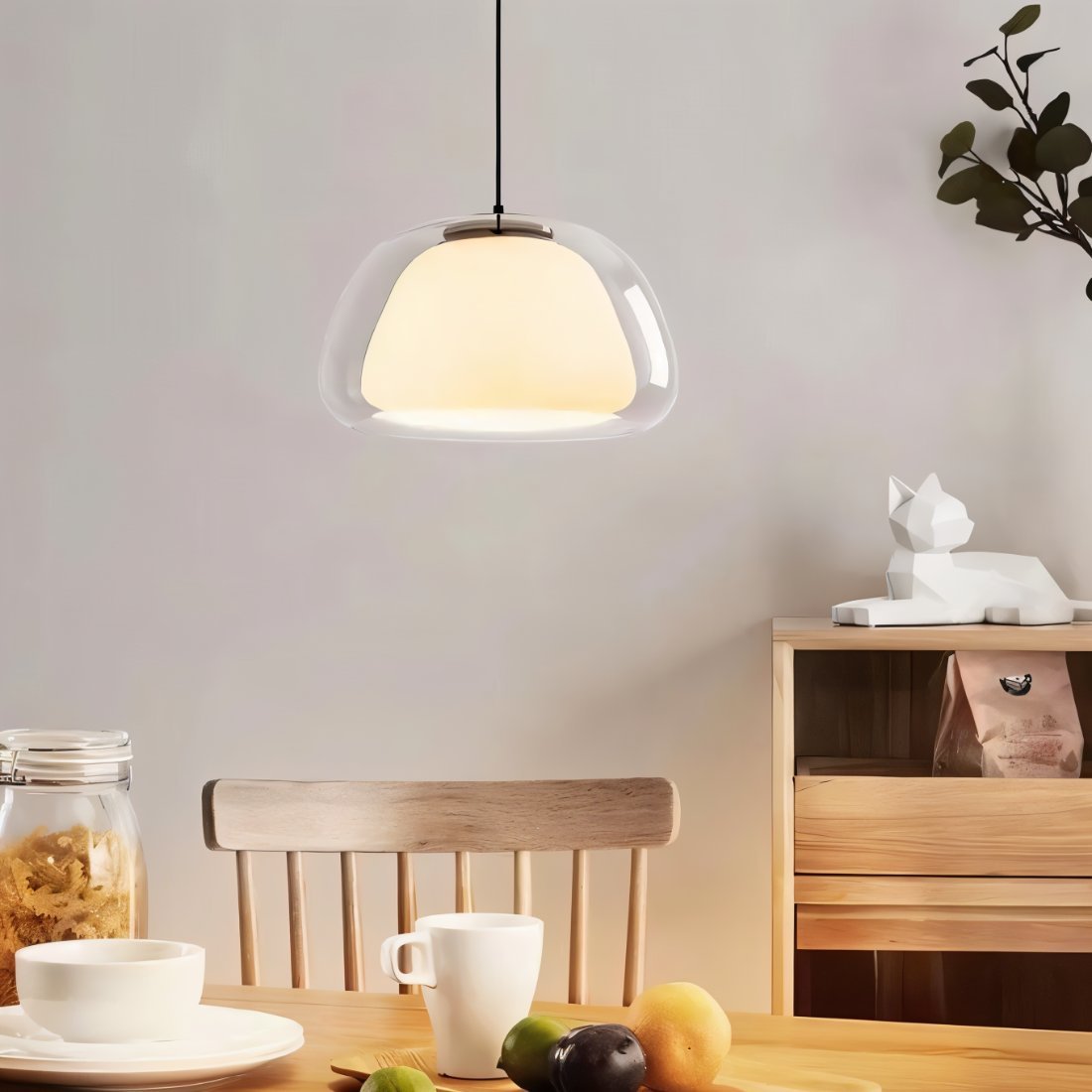Clérachic clear glass pendant light with an opal inner shade hanging above a wooden dining table set with cups and fruit.