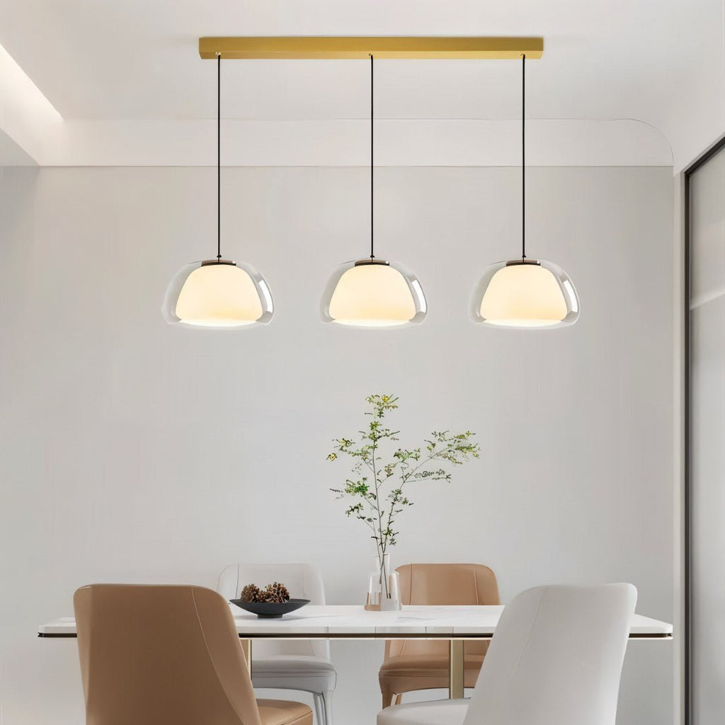 Clérachic three-head pendant light in clear glass with opal diffusers above a marble dining table with tan and white chairs.