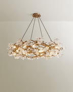 Clérachic round chandelier with gold branching metal frame and clear glass petals, hung on four cords against a pale wall.