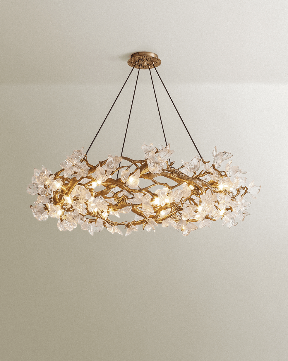 Clérachic round chandelier with gold branching metal frame and clear glass petals, hung on four cords against a pale wall.