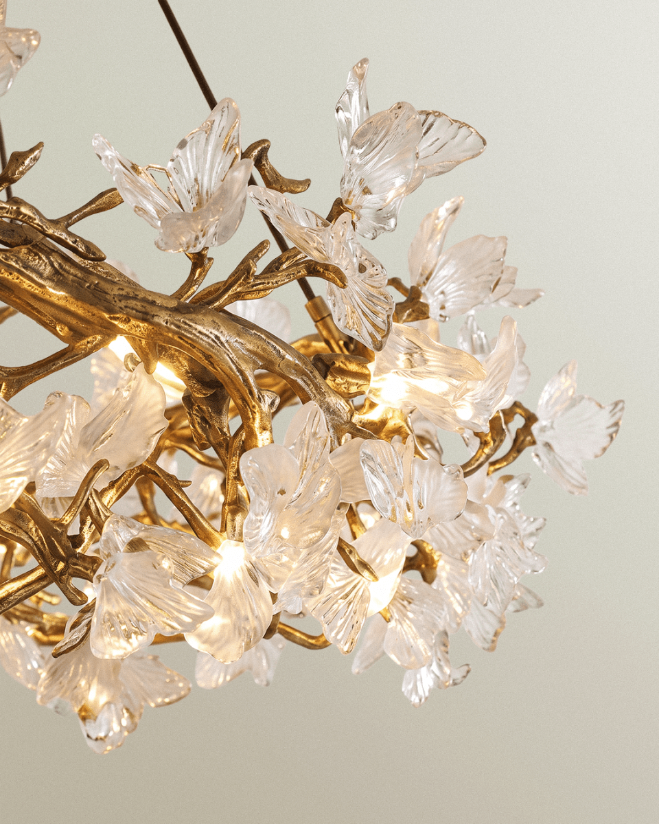 Close view of a Clérachic chandelier showing carved gold branches, lit bulbs and clear ribbed glass petals in soft light.