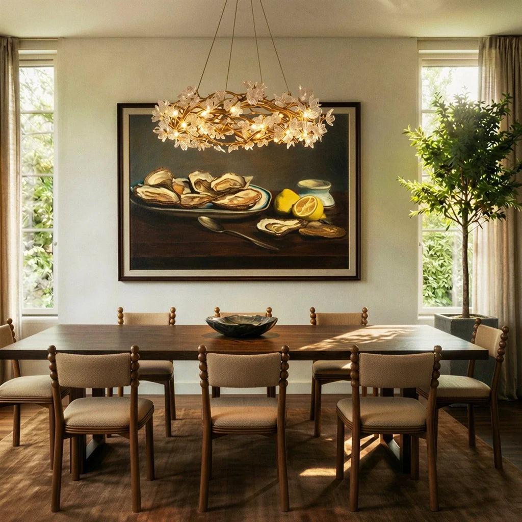 Clérachic round chandelier of gold branches and glass petals lit above a long wooden dining table in a bright dining room.