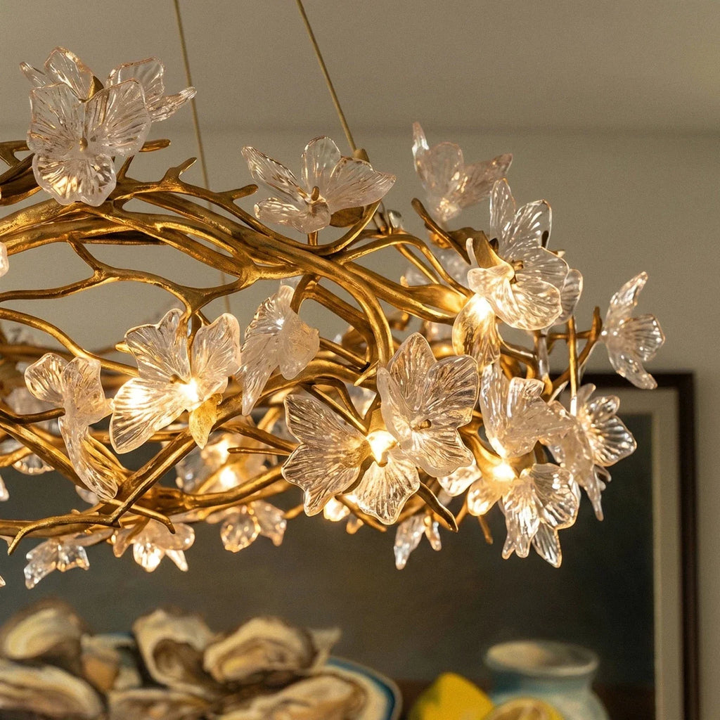 Clérachic chandelier close up, lit bulbs glowing inside clear glass petals on gold twisting branches above a dining room.