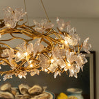 Clérachic chandelier close up, lit bulbs glowing inside clear glass petals on gold twisting branches above a dining room.