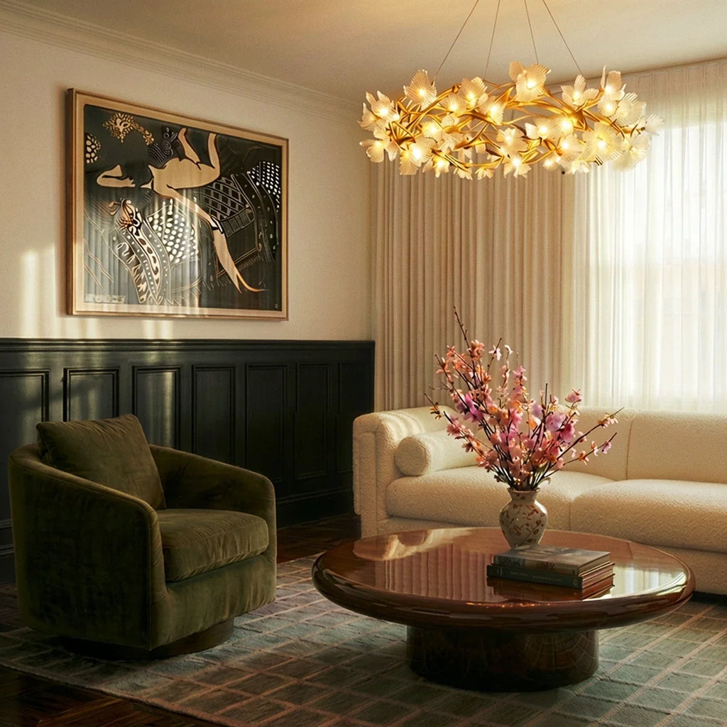 Clérachic round chandelier glowing warm above a low round coffee table in a living room with a cream sofa and green armchair.