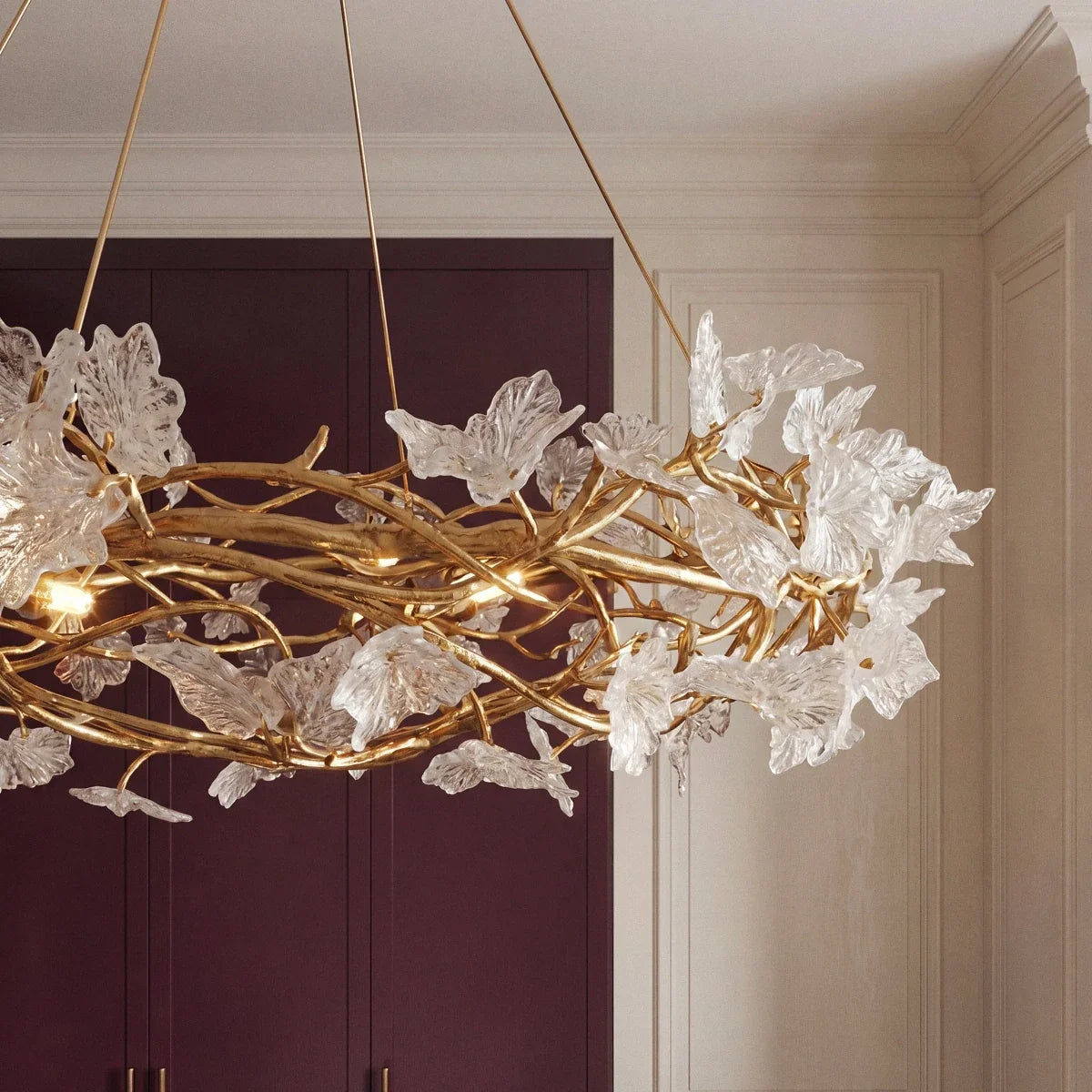 Clérachic chandelier branches and clear glass petals seen from below against plum cabinetry and cream panelled walls.