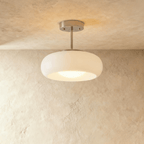 Clérachic semi-flush pendant with a rounded white glass shade on a short brushed chrome stem, softly lit against limewash.