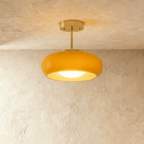 Clérachic semi-flush pendant with a rounded yellow glass shade on a short brass stem and round brass canopy, lit.