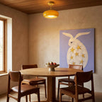 Clérachic yellow glass pendant on a brass stem above a round dining table in a warm room with a timber ceiling.