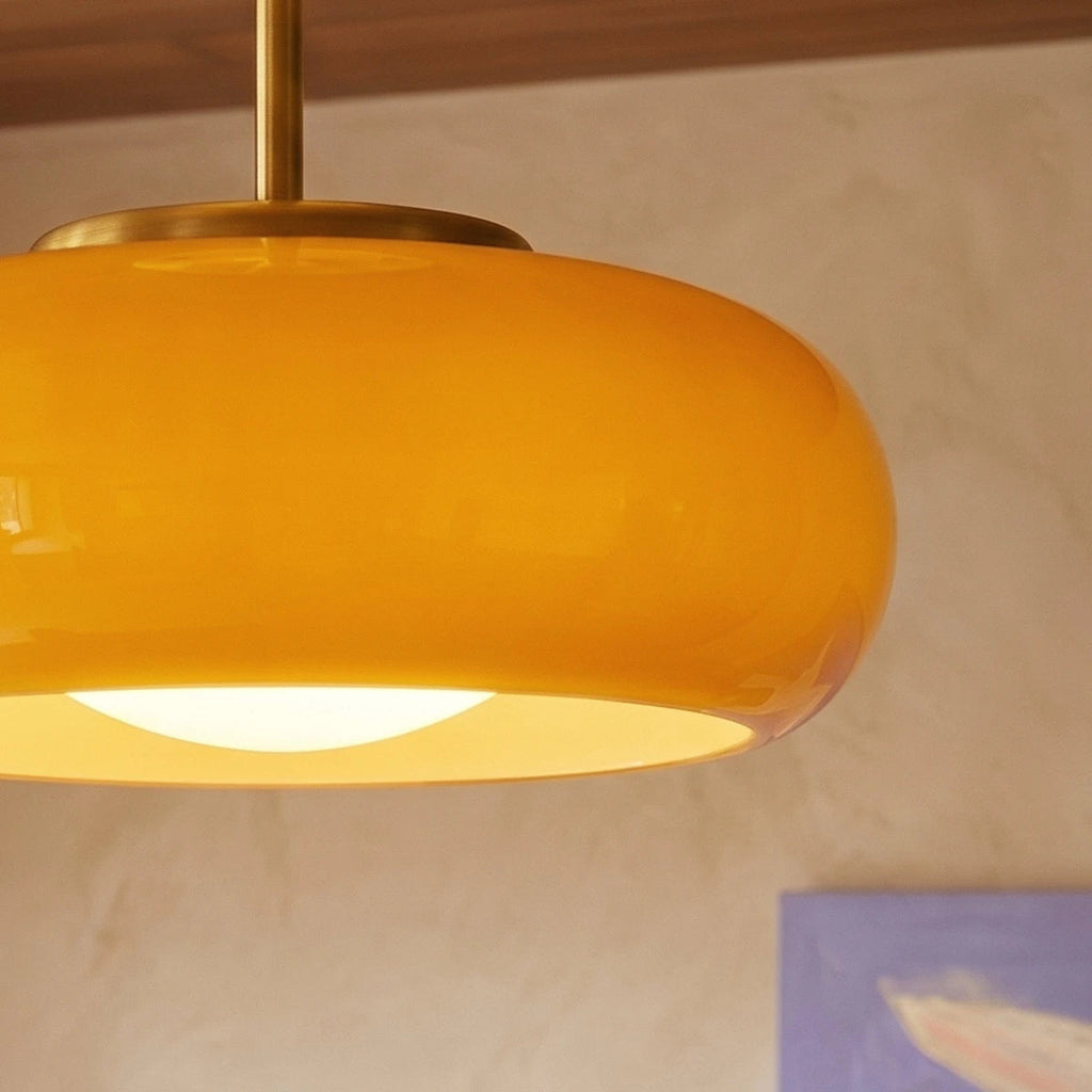 Close view of a Clérachic yellow glass shade with a brass canopy and stem, its opal bulb cover glowing in the opening.