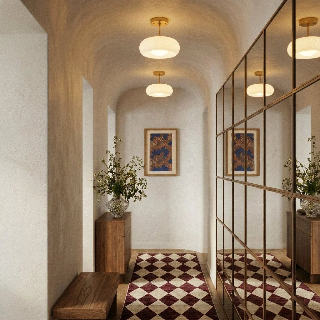 Two Clérachic white glass pendants on brass stems lighting an arched hallway with a checkered runner and mirrored wall.