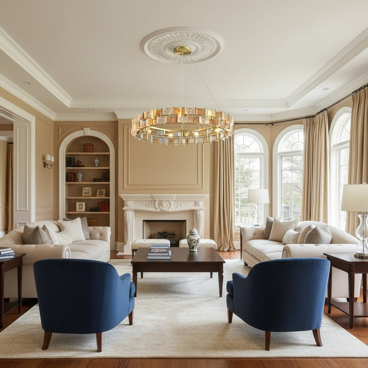 An amber Clérachic chandelier hangs from a ceiling rose in a traditional living room with navy armchairs, cream sofas and arched windows.