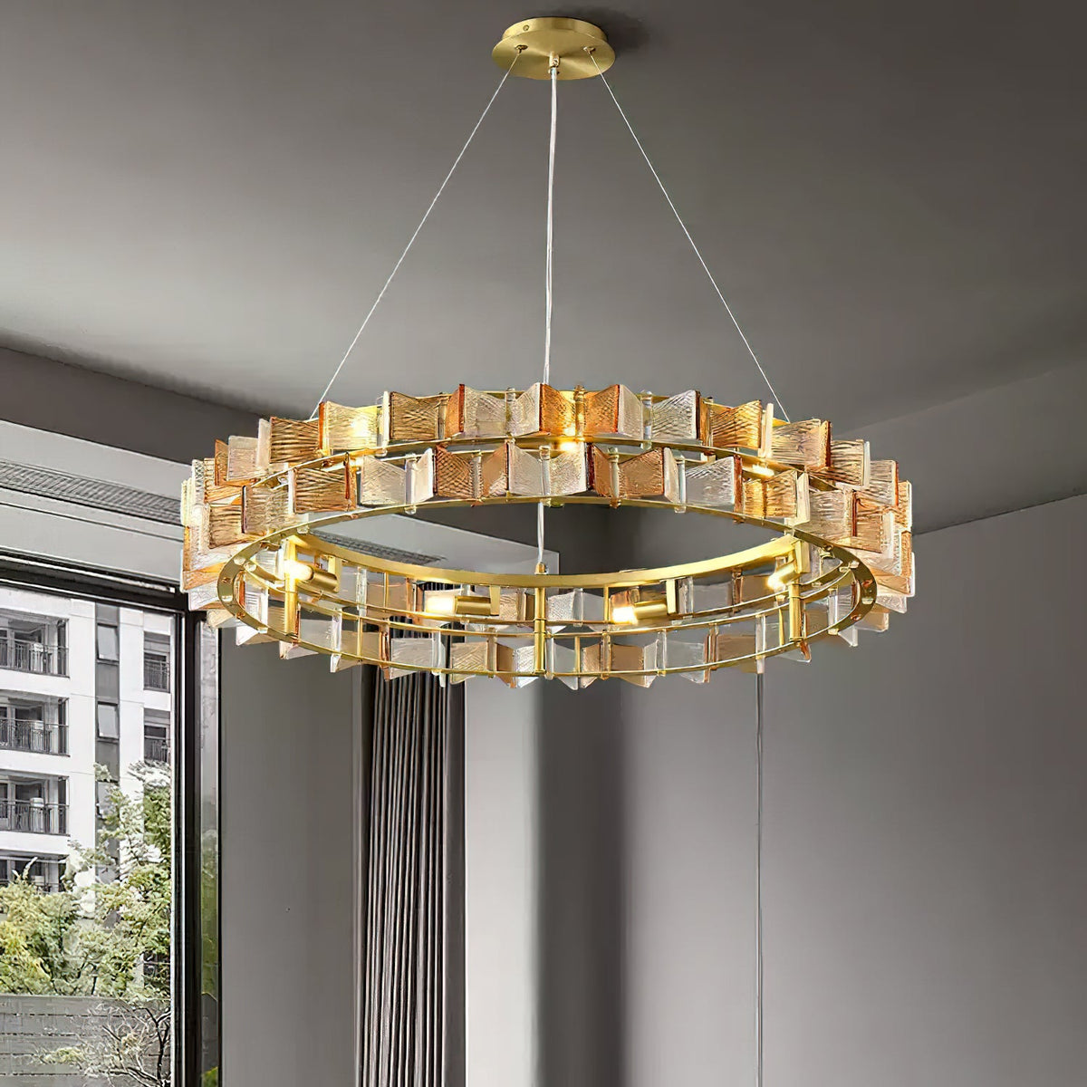 Seen from below, this amber Clérachic chandelier shows its brass ring and two tiers of ribbed glass against a dark grey wall.