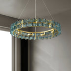 Looking up at a blue Clérachic chandelier, its brass ring and ribbed glass blades lit from inside, against a grey wall and pale window.