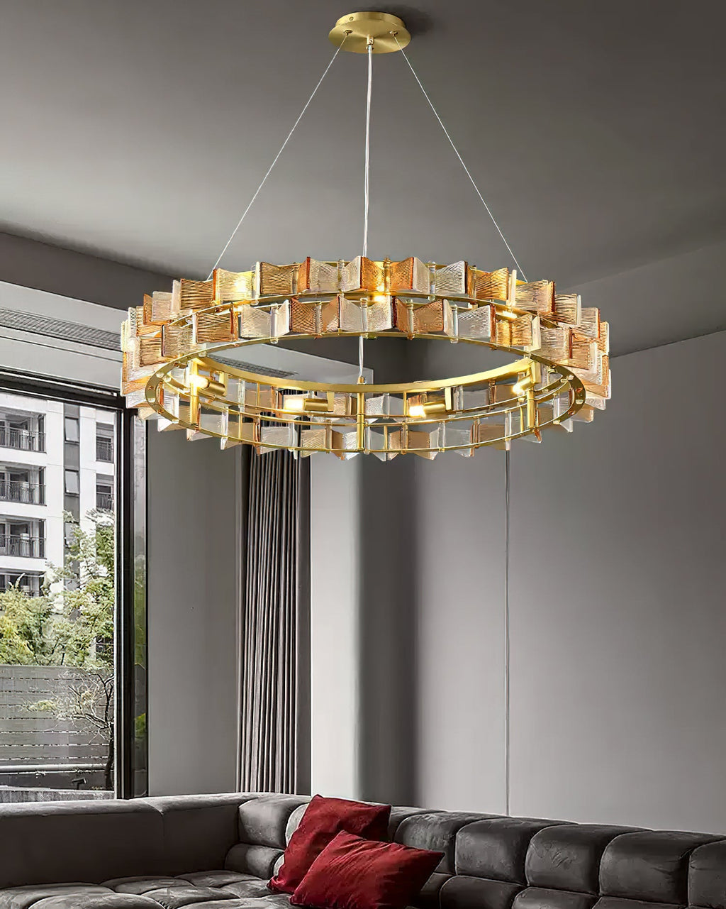 A wider view of an amber Clérachic chandelier above a tufted sofa with red cushions, with a tall window at the left.