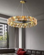A wider view of an amber Clérachic chandelier above a tufted sofa with red cushions, with a tall window at the left.