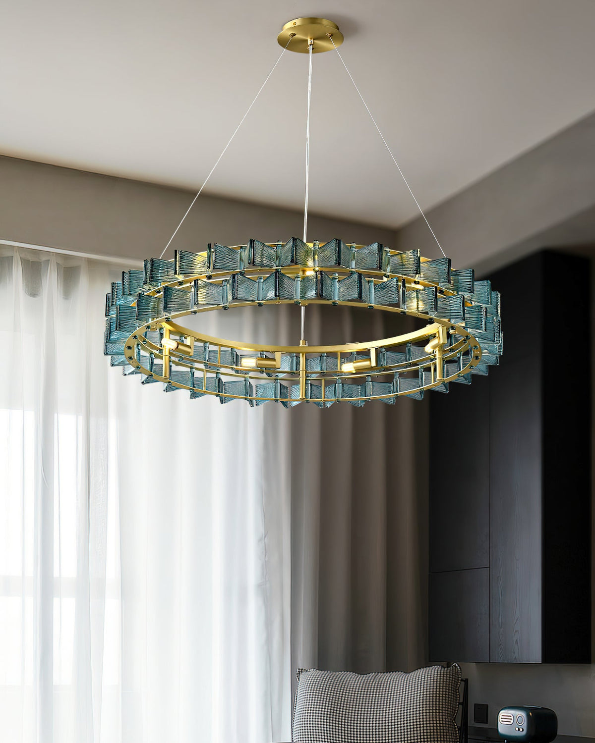 Blue glass blades on this Clérachic chandelier glow against a grey ceiling, with sheer curtains and a dark wardrobe behind.