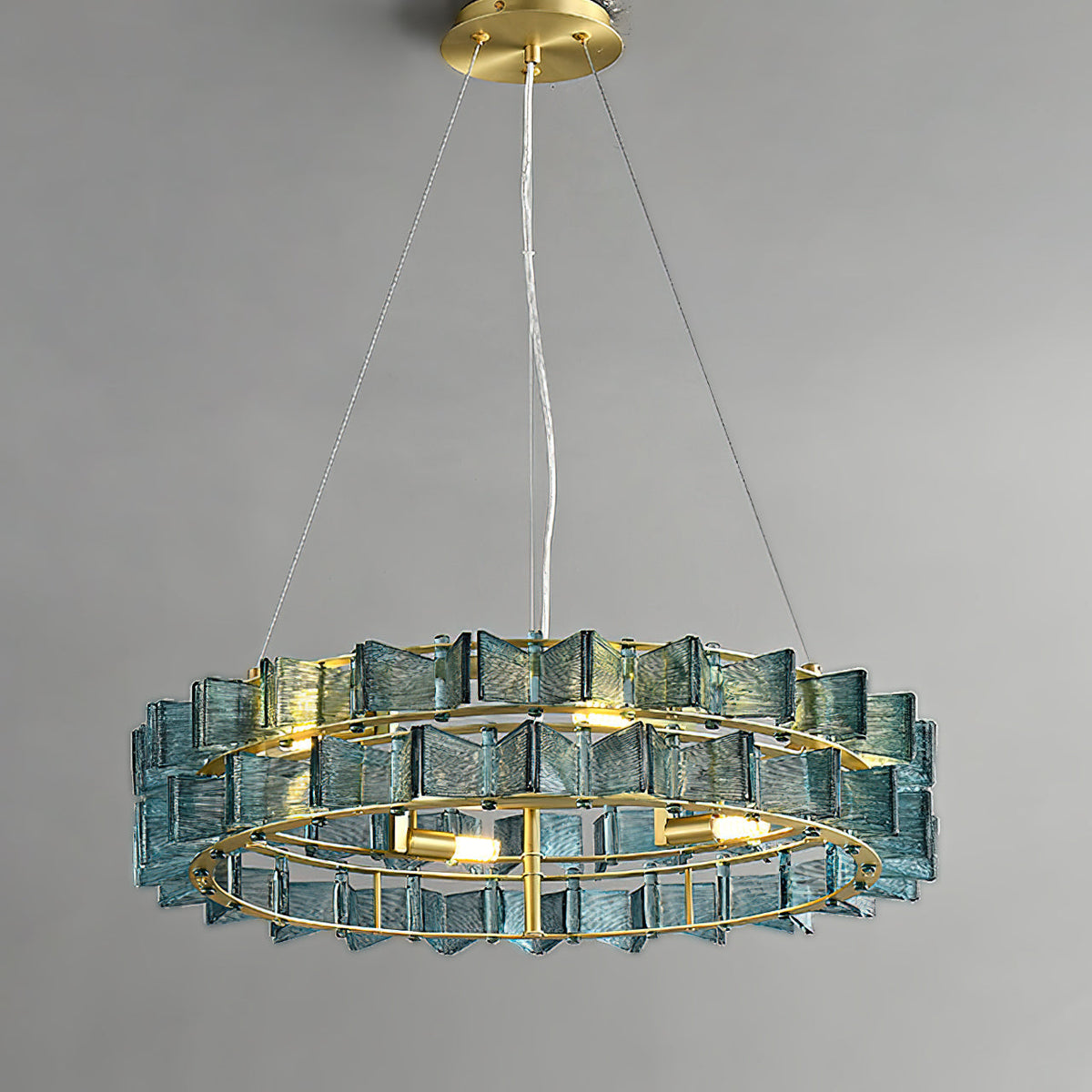 Slightly lower angle on a blue Clérachic chandelier, its bulbs glowing inside the brass ring of ribbed glass blades.
