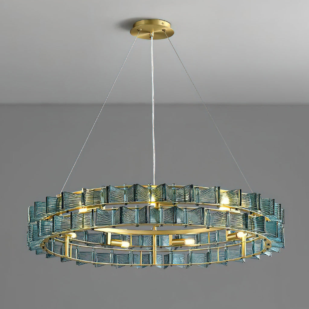 Lit blue Clérachic chandelier on a grey backdrop, its brass ring and spaced bulbs visible beneath two rows of ribbed glass.