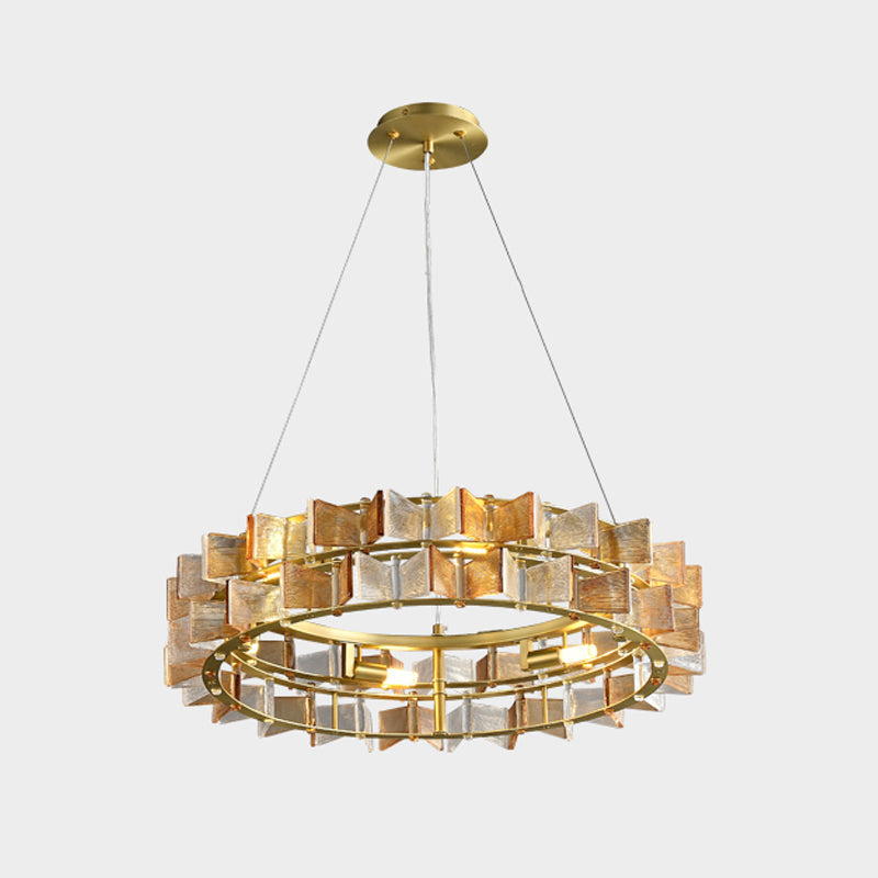 An amber Clérachic chandelier on light grey, its glass blades in warm tones around the brass ring and the lit bulbs.