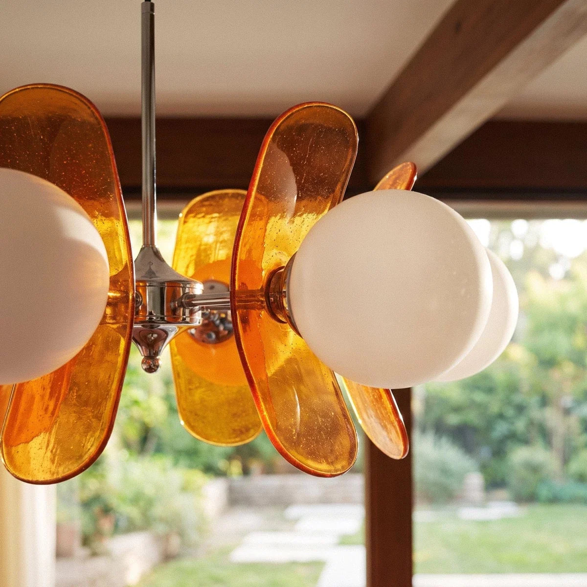 Close view of Clérachic orange bubbled acrylic petals and opal glass globes on a chrome hub, garden behind