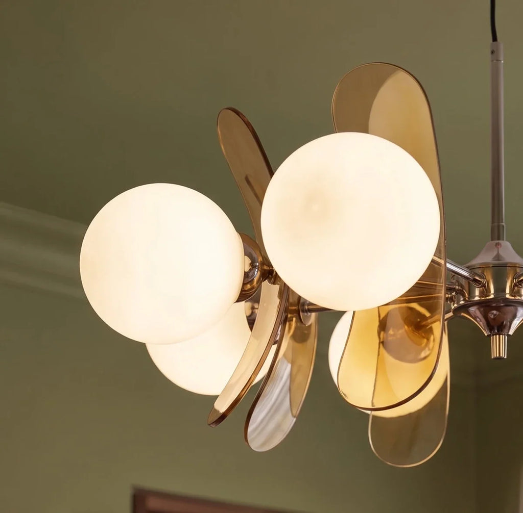 Clérachic chandelier detail, warm opal globes and tinted brown acrylic petals against an olive green wall