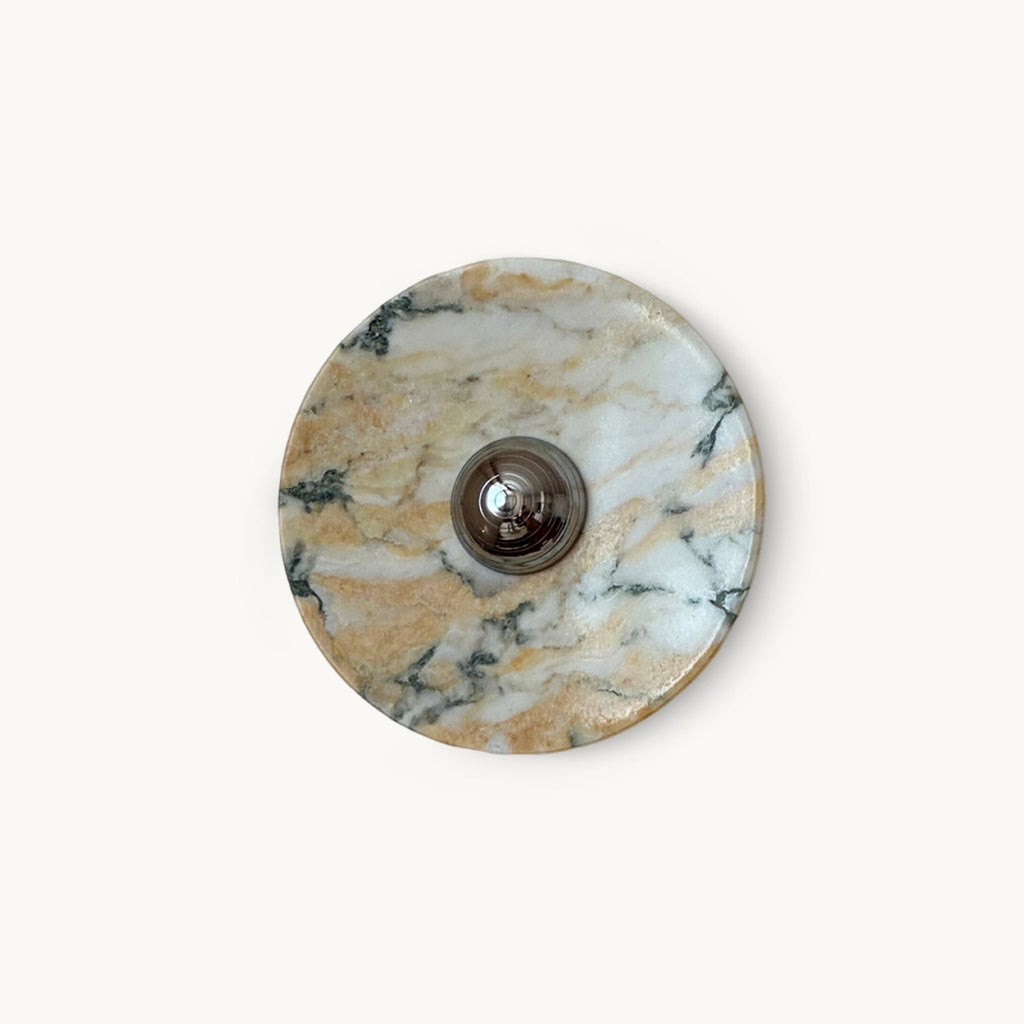 A round Clérachic marble wall light with warm gold and white veining and a chrome dome at its centre, on a plain white backdrop.