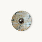 A round Clérachic marble wall light with warm gold and white veining and a chrome dome at its centre, on a plain white backdrop.