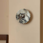 Unlit, this Clérachic round marble wall light shows plum, black and white veining around its chrome centre on a warm cream wall.