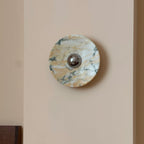 A Clérachic marble wall light switched off, its stone warm gold and white with fine green veins, on a peach-cream wall.