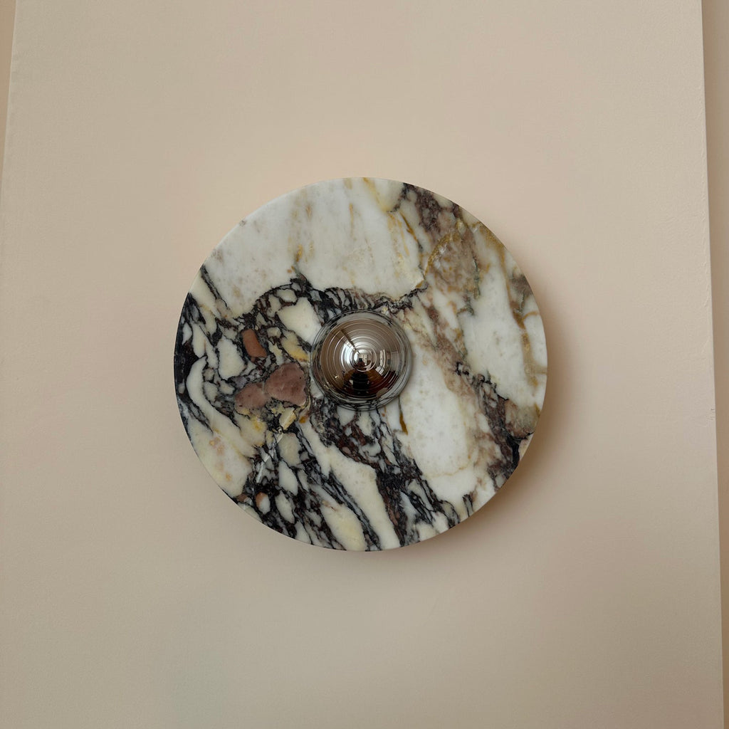 Close view of a Clérachic round marble wall light with black, plum and cream veining around a polished chrome dome.