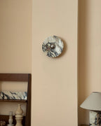 A Clérachic marble wall light unlit on a cream panel, with dark veins and cream patches around its chrome dome and shelving below.