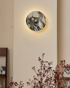 A lit Clérachic marble wall light above a bare branch with red berries, with a glow around the stone's edge on a cream wall.