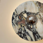 Very close view of a Clérachic marble wall light, with its polished chrome dome and black, plum and gold veins lit from behind.