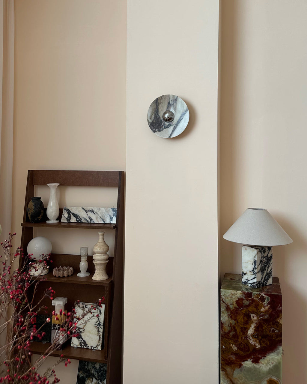 The same Clérachic wall light unlit, its chrome dome catching the room, above a shelf of stone vases and a marble-based lamp.