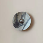 A close front view of the Clérachic wall light in grey and white marble, with a dark diagonal vein running past the chrome dome.