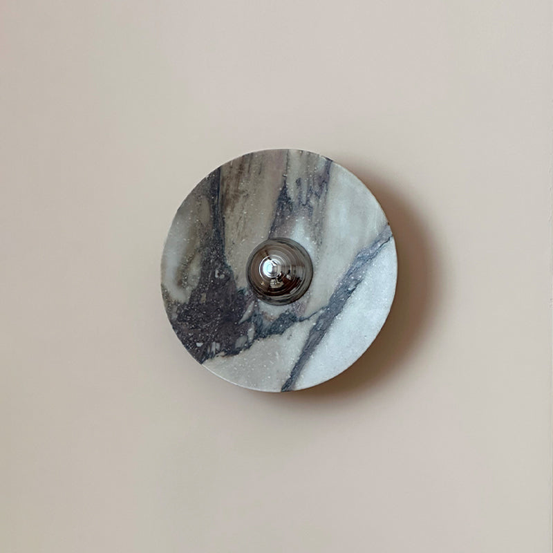 A close front view of the Clérachic wall light in grey and white marble, with a dark diagonal vein running past the chrome dome.